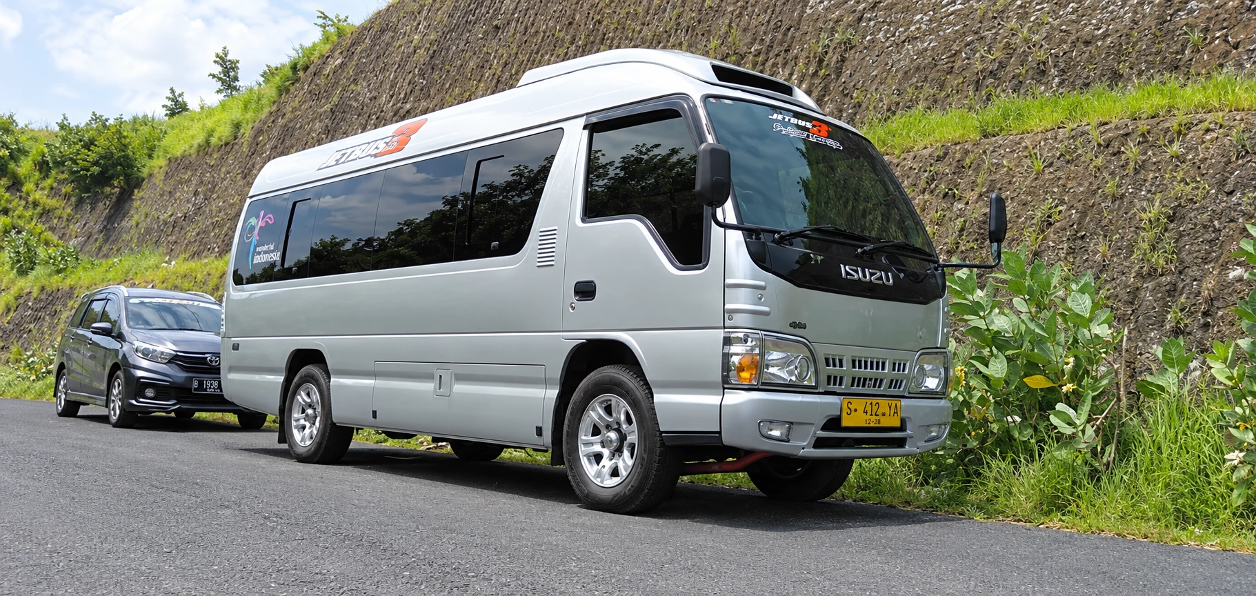 Isuzu Elf Long warna silver di jalan perbukitan